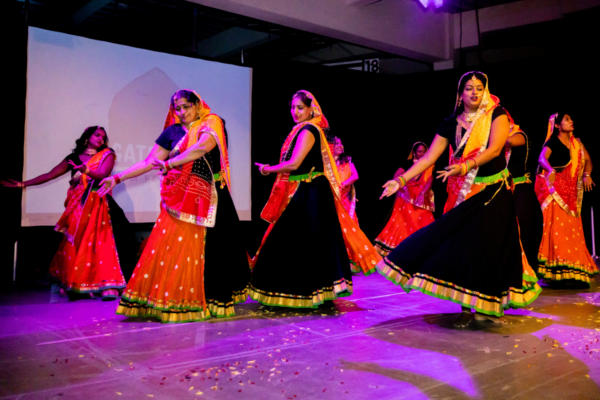 Dancers in South Asian dress perform in front of cinema screen.