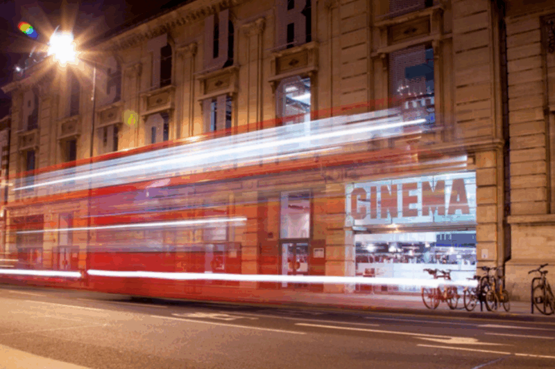 Long exposure photo of a bus passing a cinema at night.