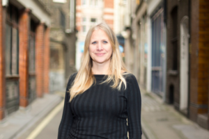Headshot of Catharine Des Forges on a narrow street. She is middle aged blonde woman.