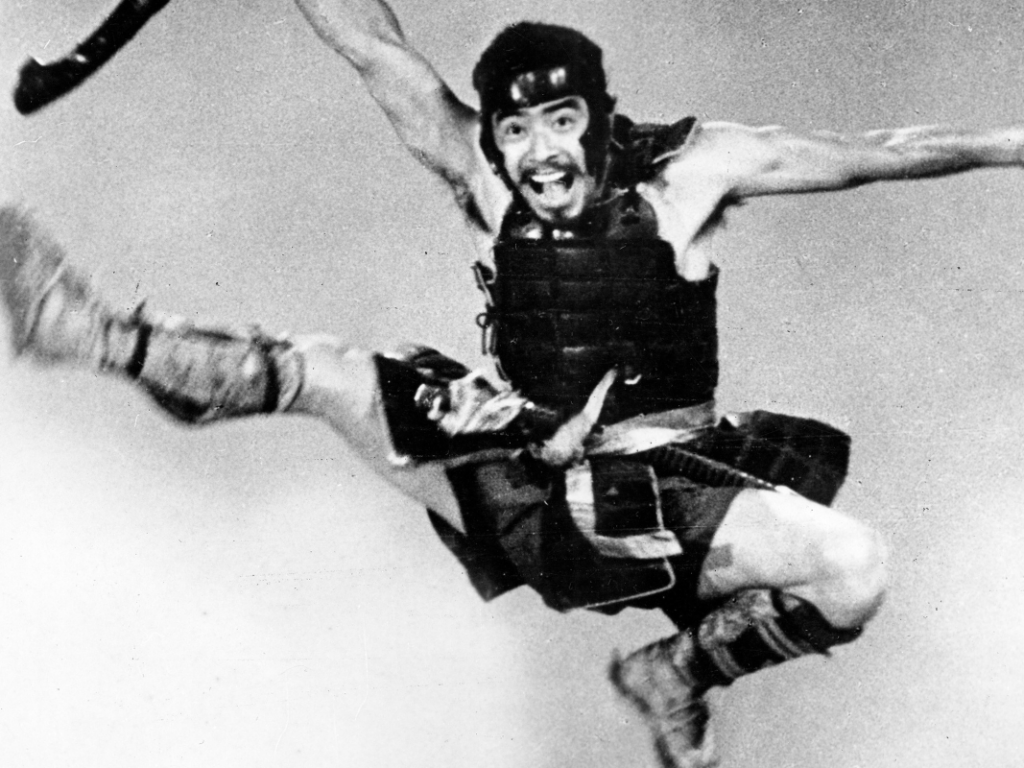 Black and white film still of a man in Samurai dress hanging in the air in a martial arts pose.
