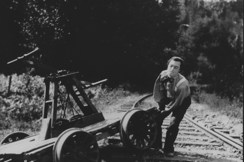 Black and white film still of Buster Keaton handling equipment on a railway track.