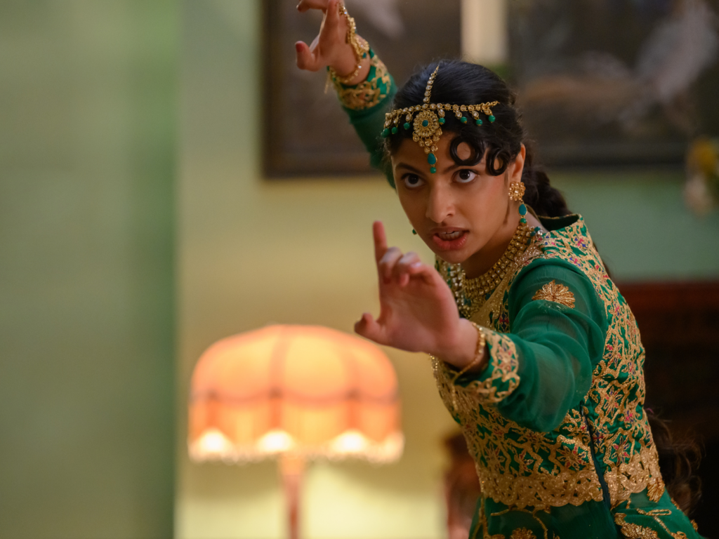 A young woman in South Asian dress hits a martial arts pose in front of a lamp.