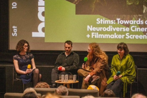A panel event a the Barbican. Four people sit, holding microphones, with an event slide projected behind them.